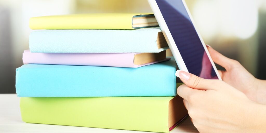 Woman's hand holding a digital tablet beside books, representing digital learning, research, or online education.