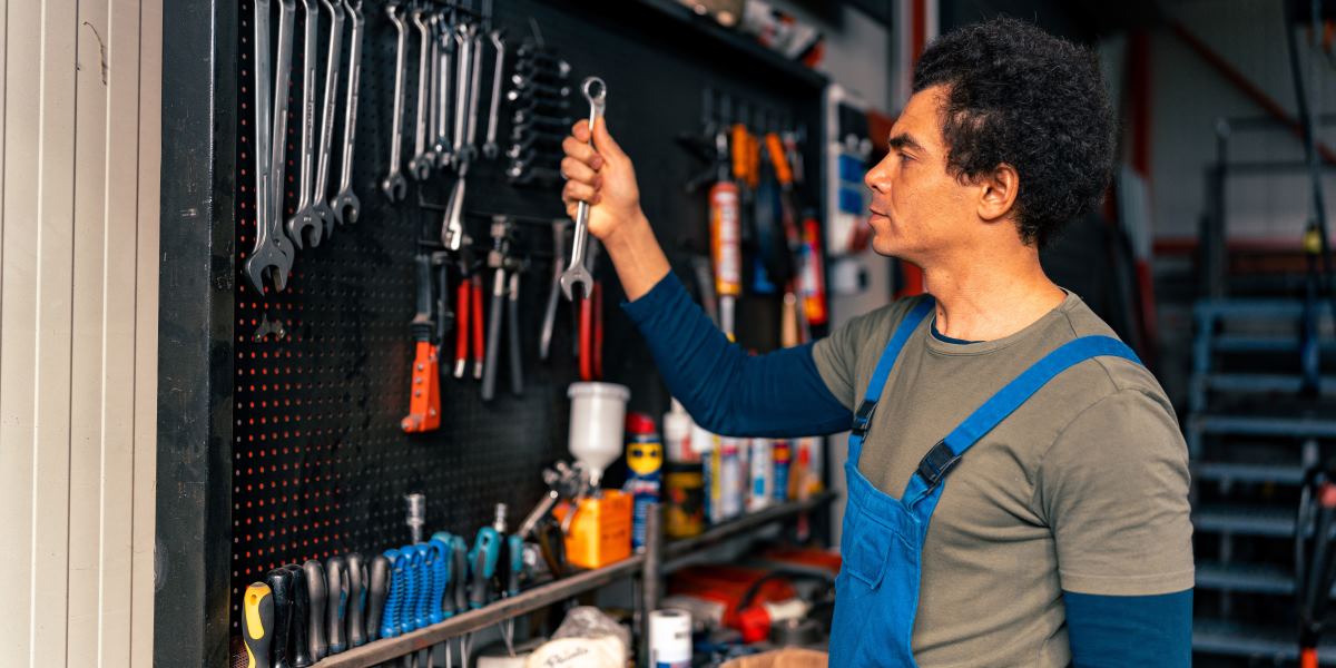 Skilled technician in overalls organizing hand tools on a workshop wall for efficient storage and easy access.