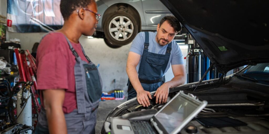 Mechanics using diagnostic software to inspect and troubleshoot a car engine in an automotive repair workshop.