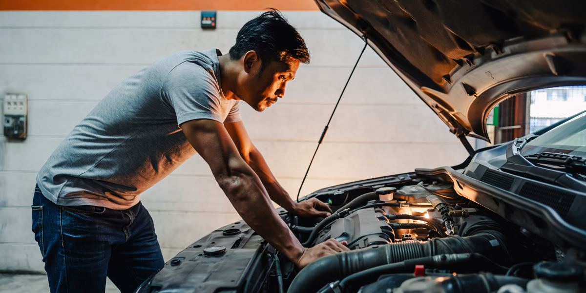 Mechanic inspecting a car engine under the hood in a garage or workshop.