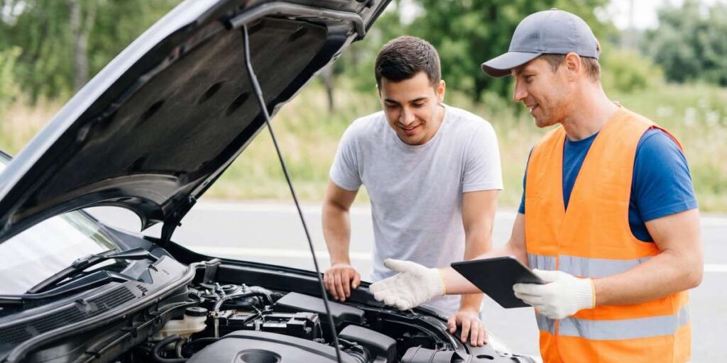 Car mechanic and vehicle owner inspecting a car engine together while discussing maintenance and repair.