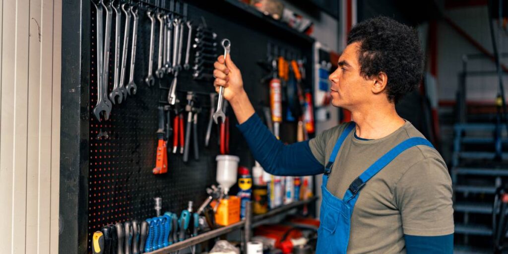 Skilled technician in overalls organizing hand tools on a workshop wall for efficient storage and easy access.