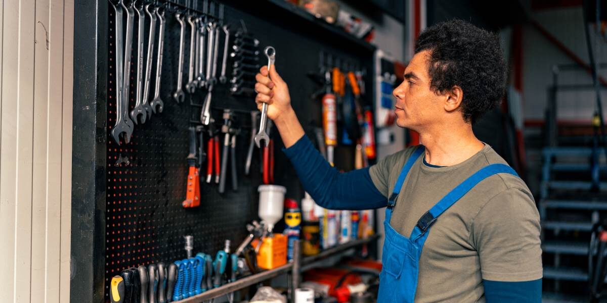 Skilled technician in overalls organizing hand tools on a workshop wall for efficient storage and easy access.