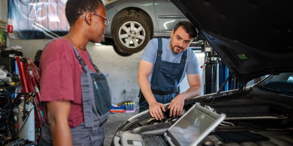 Mechanics using diagnostic software to inspect and troubleshoot a car engine in an automotive repair workshop.