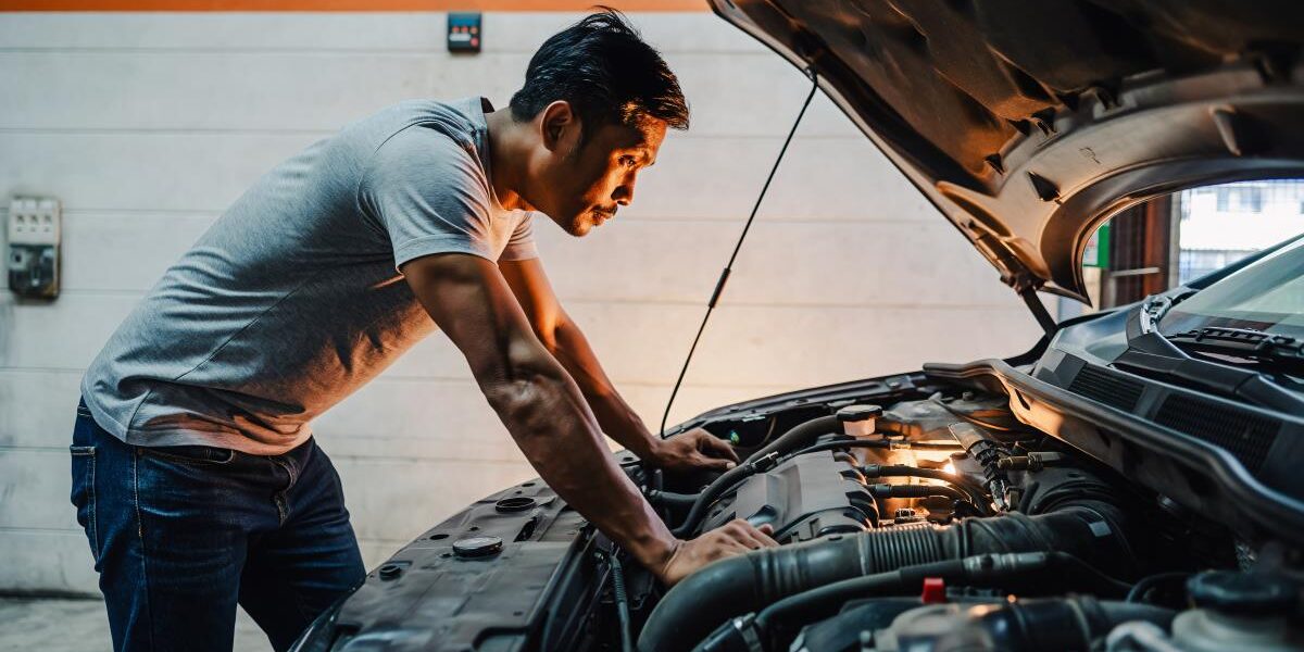 Mechanic inspecting a car engine under the hood in a garage or workshop.