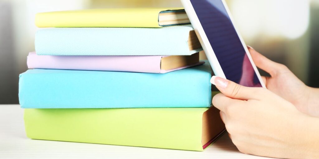 Woman's hand holding a digital tablet beside books, representing digital learning, research, or online education.