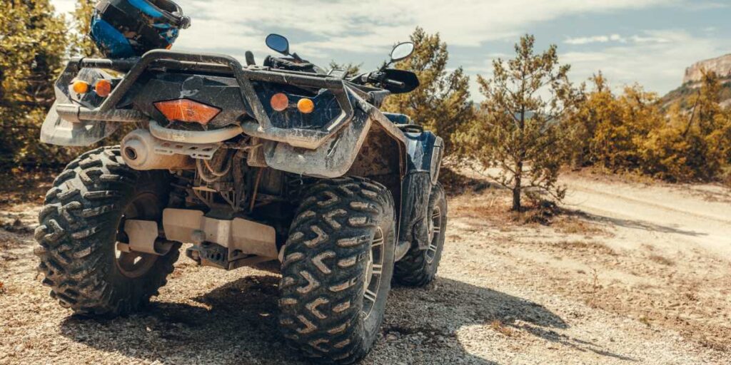 Dirty ATV parked in the middle of a desert with a helmet in the back.