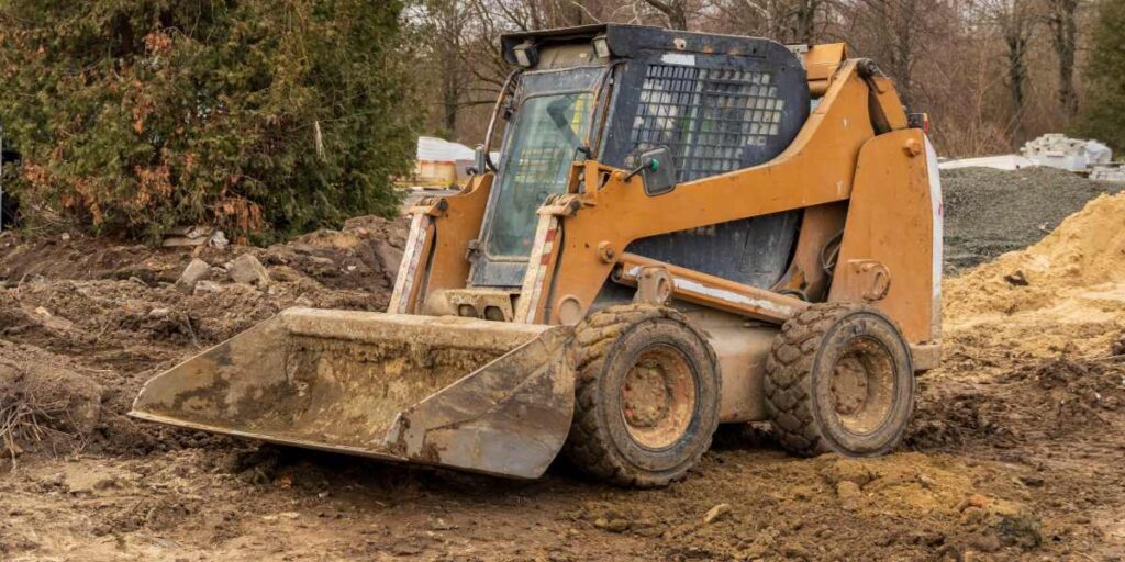 Orange skid steer loader parked on muddy ground.