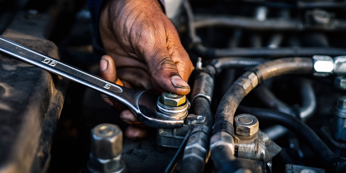 Mechanic tightening a bolt on a car engine with a wrench during maintenance and repair.