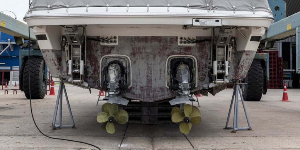 Back view of the motorboat with two outboard motors in the shipyard, being lifted by an industrial crane.